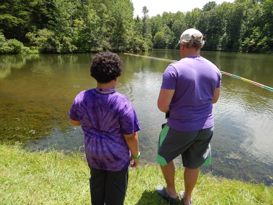 A camper and a counselor walking together along the pond