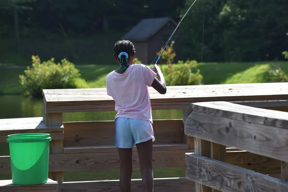 A camper fishing at the edge of the pond, bucket beside him